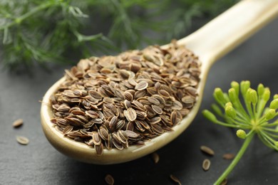 Photo of Spoon with dry seeds and fresh dill on black table, closeup