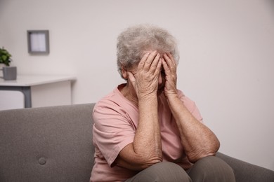 Photo of Senior woman with headache sitting on sofa at home