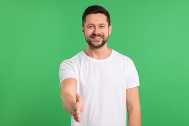 Photo of Happy man welcoming and offering handshake on green background