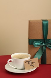 Photo of Happy Father's Day. Coffee cup, card with greetings and gift box on red table