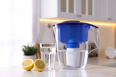 Water filter jug, glass and lemon on white marble table in kitchen, closeup