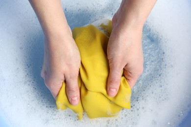 Photo of Top view of woman hand washing color clothing in suds, closeup