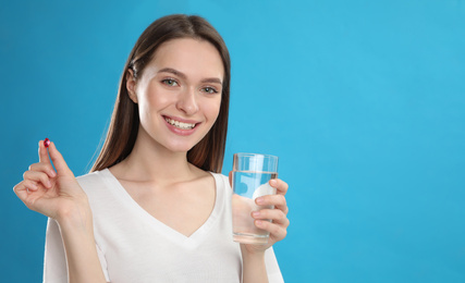 Photo of Young woman with vitamin pill and glass of water on blue background