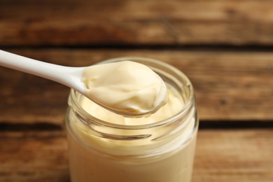 Delicious mayonnaise and spoon in glass jar on wooden table, closeup