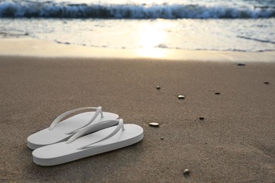 Stylish white flip flops on sand near sea. Space for text