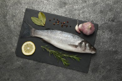 Sea bass fish and ingredients on grey table, top view