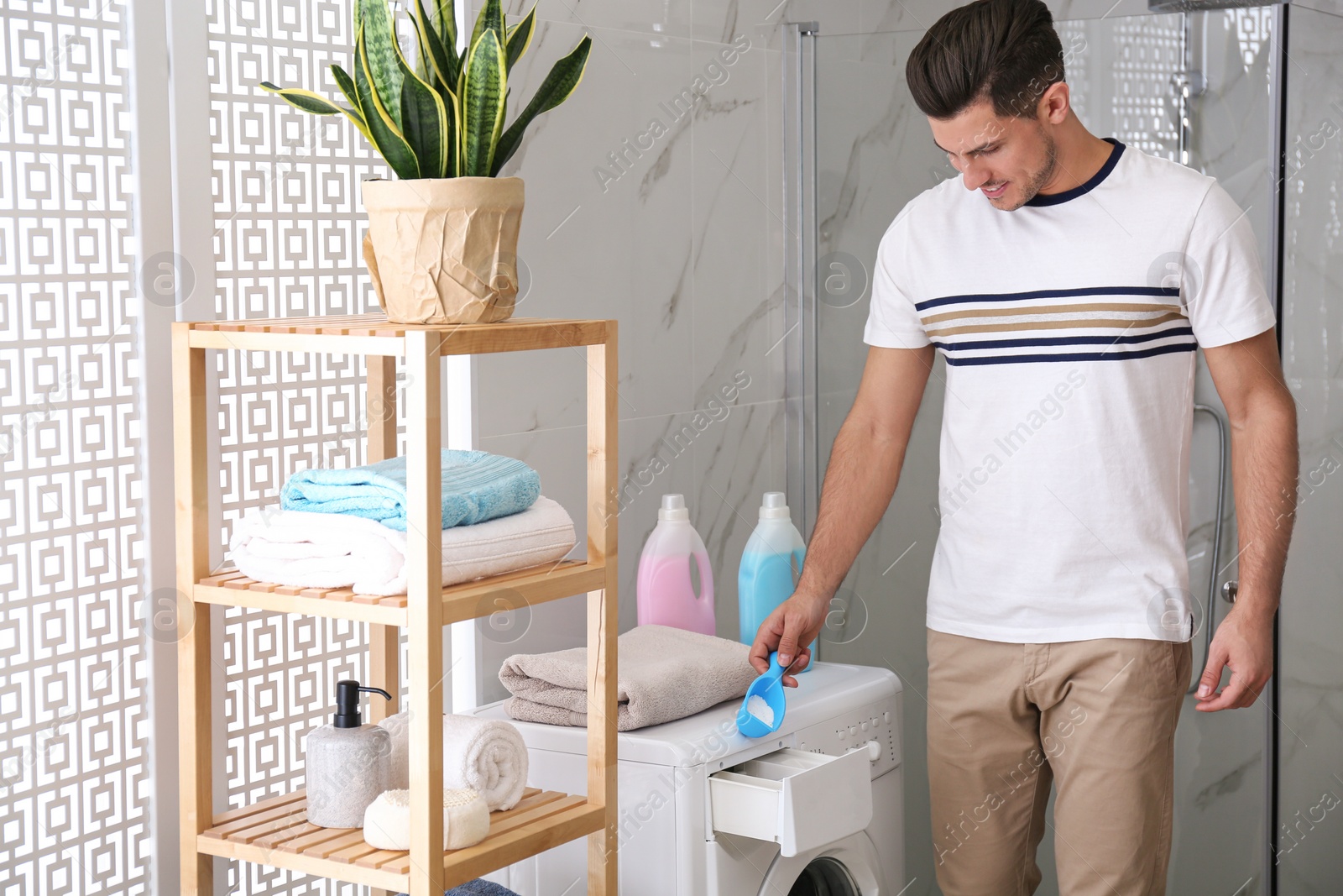 Photo of Man pouring laundry detergent into washing machine drawer in bathroom