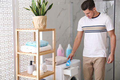 Man pouring laundry detergent into washing machine drawer in bathroom