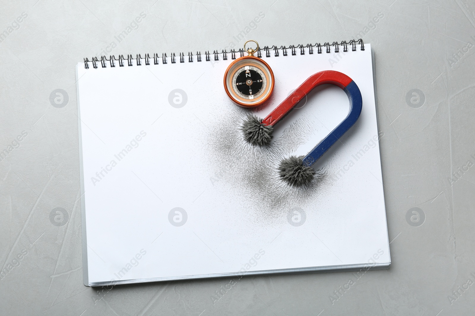 Photo of Notebook, compass and magnet with iron powder on grey background, top view. Space for text