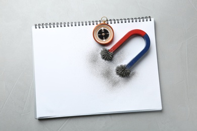 Notebook, compass and magnet with iron powder on grey background, top view. Space for text