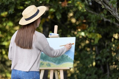Photo of Young woman drawing on easel in forest, back view