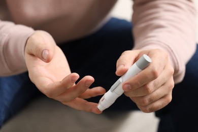 Photo of Diabetes test. Man checking blood sugar level with lancet pen on blurred background, closeup