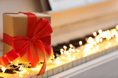 Photo of Gift box and fairy lights on piano keys, space for text. Christmas music