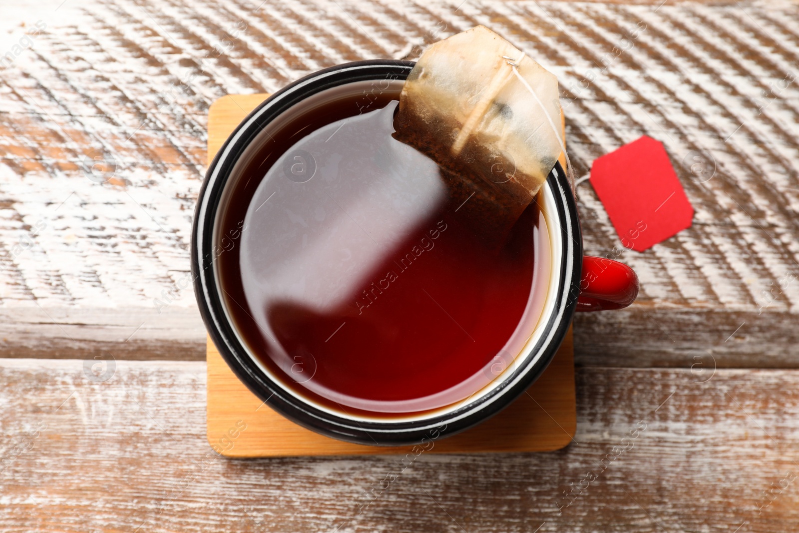 Photo of Tea bag in cup with hot drink on wooden rustic table, top view