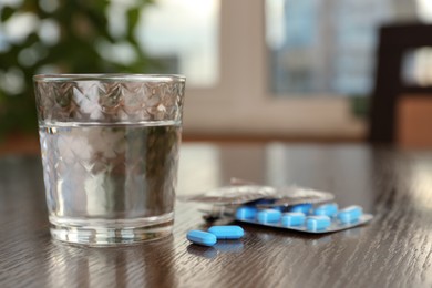 Photo of Glass of water, condoms and pills on wooden table indoors, space for text. Potency problem concept