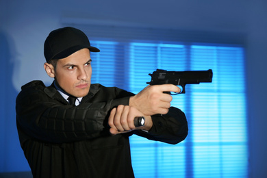 Photo of Professional security guard with flashlight and gun in dark room