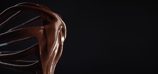 Image of Whisk with yummy chocolate cream on black background, closeup. Banner design with space for text