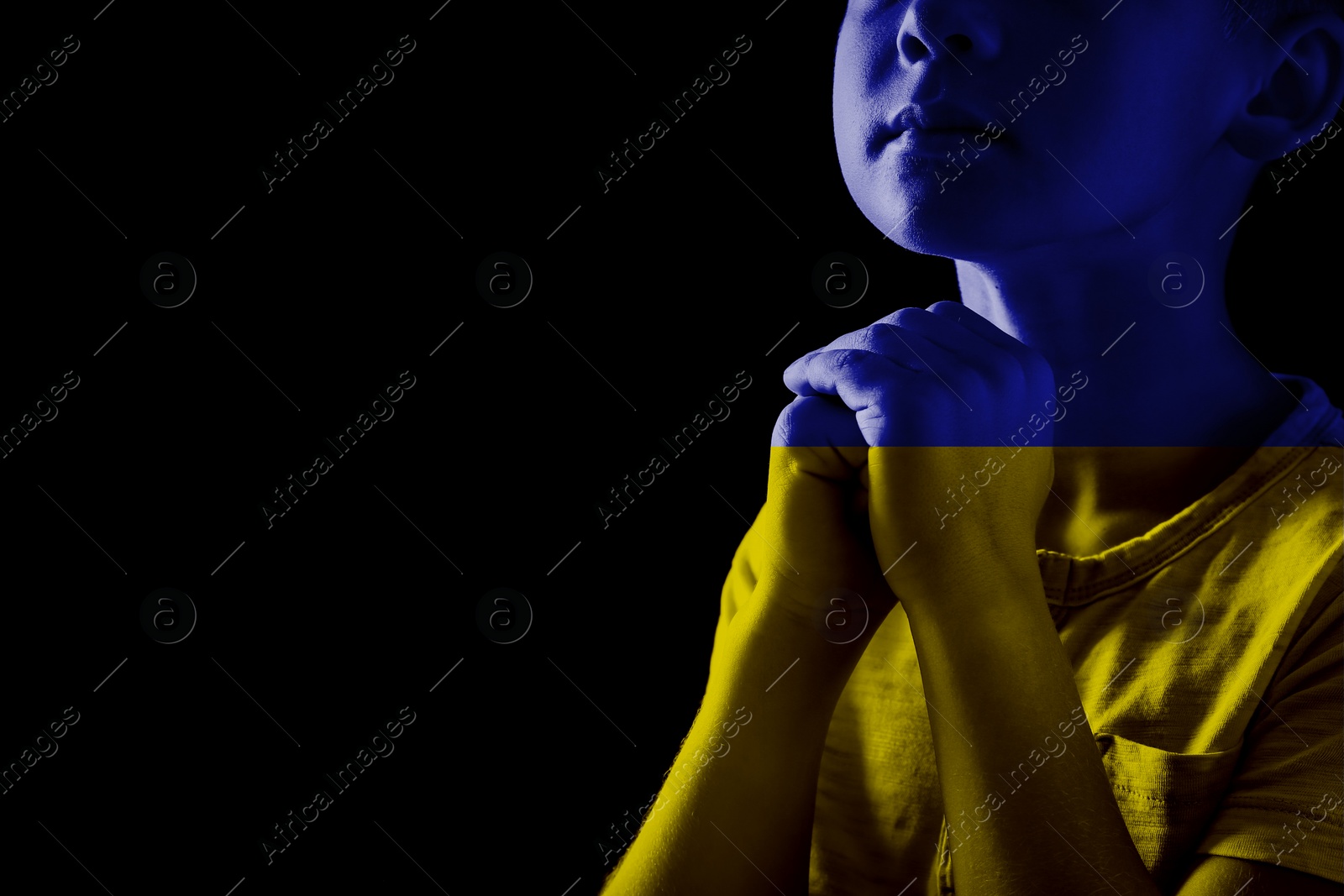 Image of Pray for Ukraine. Double exposure of little boy praying on black background and Ukrainian national flag