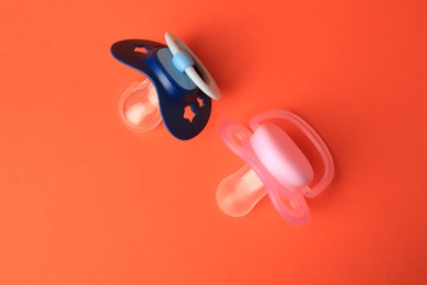 Photo of Colorful baby pacifiers on orange background, flat lay