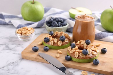 Photo of Fresh green apples with peanut butter, blueberries and nuts on white marble table