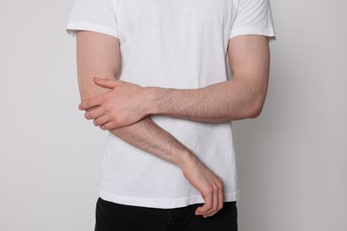 Photo of Man suffering from pain in his elbow on light background, closeup. Arthritis symptoms