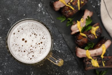 Photo of Mug with beer and delicious grilled ribs on dark grey textured table, closeup. Space for text