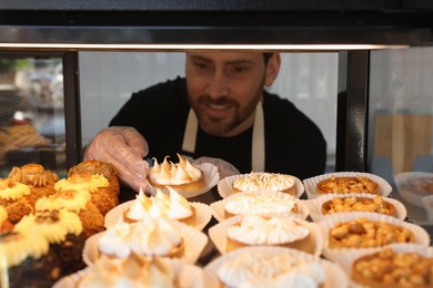 Photo of Seller taking tasty tartlet from showcase in bakery shop