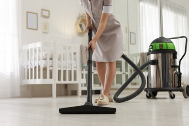 Photo of Professional chambermaid vacuuming floor in nursery, closeup