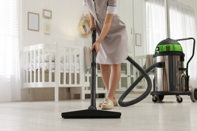 Professional chambermaid vacuuming floor in nursery, closeup