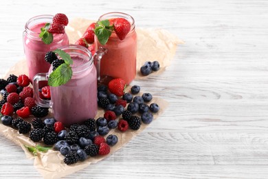 Mason jars of different berry smoothies and fresh ingredients on white wooden table. Space for text