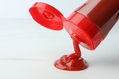 Photo of Pouring tasty red ketchup from bottle on white background, closeup