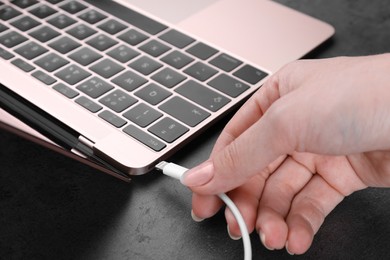 Photo of Woman plugging USB cable with lightning connector into laptop port on dark table, closeup
