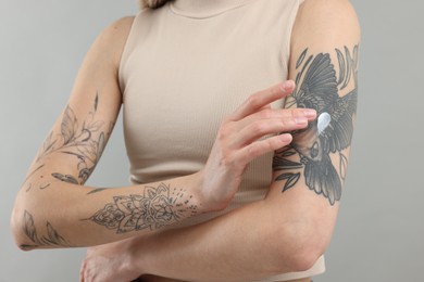 Photo of Tattooed woman applying cream onto her arm on gray background, closeup