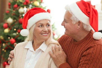 Happy mature couple in Santa hats at home. Christmas celebration