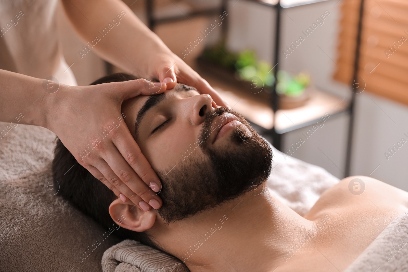 Photo of Young man receiving facial massage in beauty salon