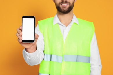 Man in reflective uniform showing smartphone on orange background, closeup