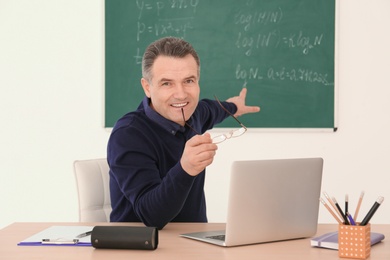 Male teacher working with laptop at table in classroom