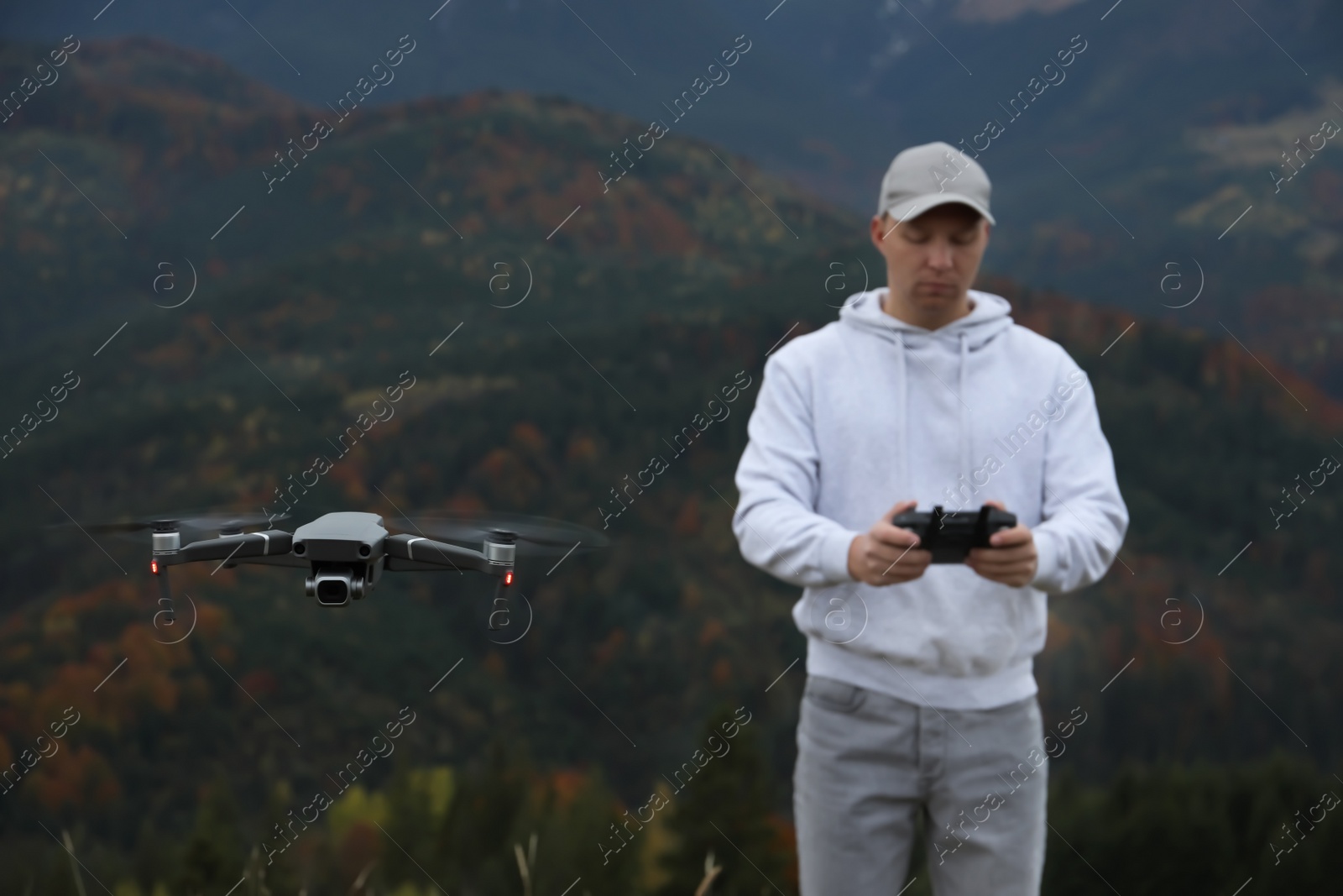 Photo of Young man operating modern drone with remote control in mountains