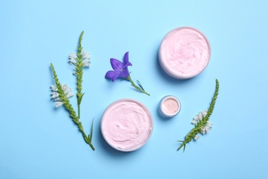 Flat lay composition with jars of body cream and flowers on light blue background