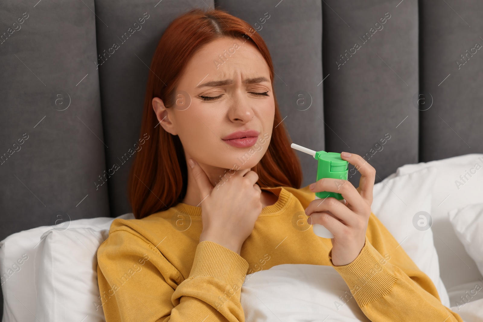 Photo of Young woman holding throat spray in bed