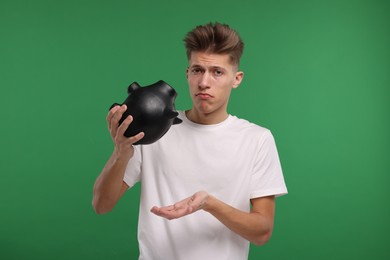 Upset man with empty piggy bank on green background