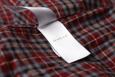 Photo of Clothing label on beautiful checkered garment, closeup
