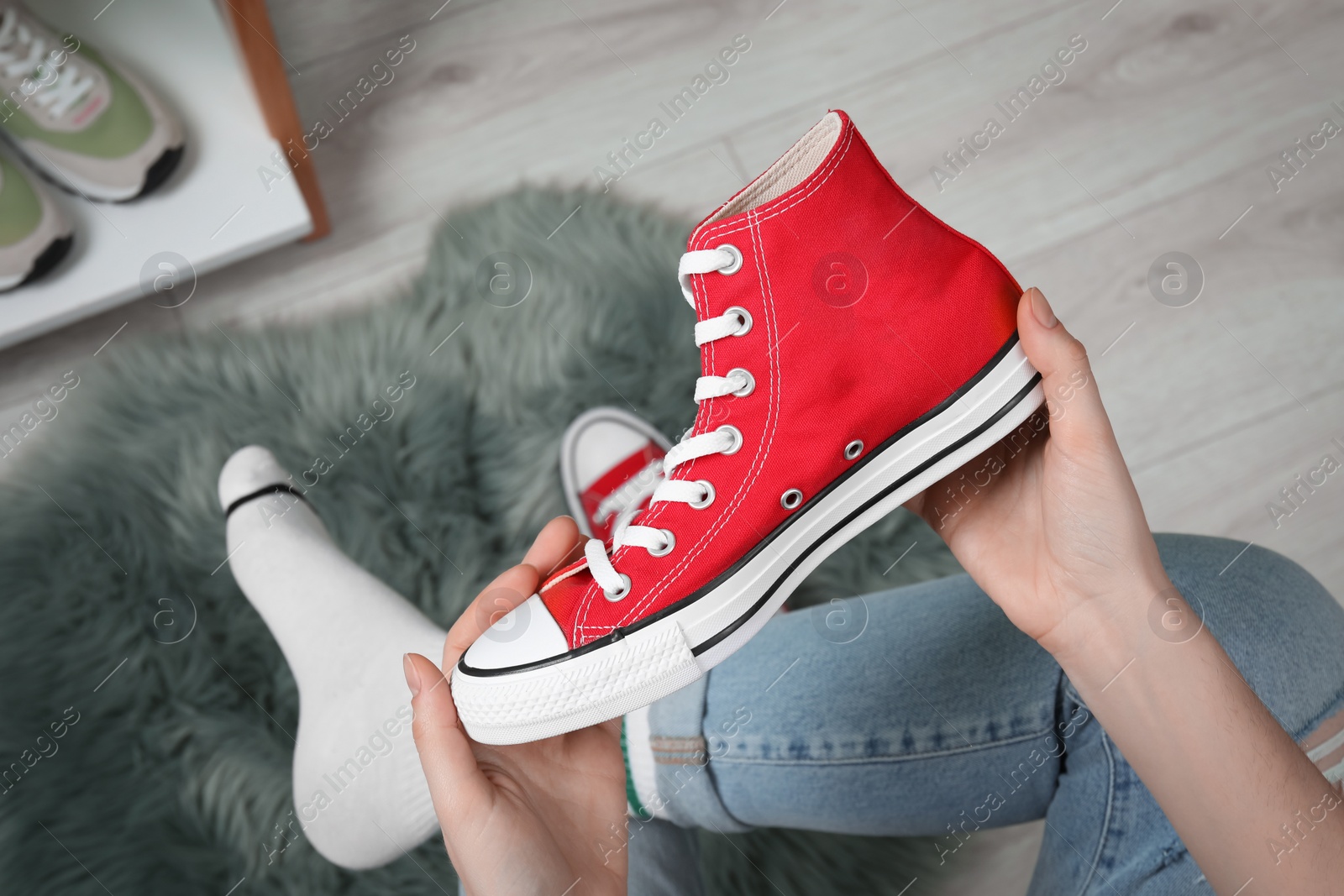 Photo of Woman holding new stylish red sneaker indoors, top view