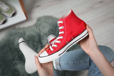 Woman holding new stylish red sneaker indoors, top view