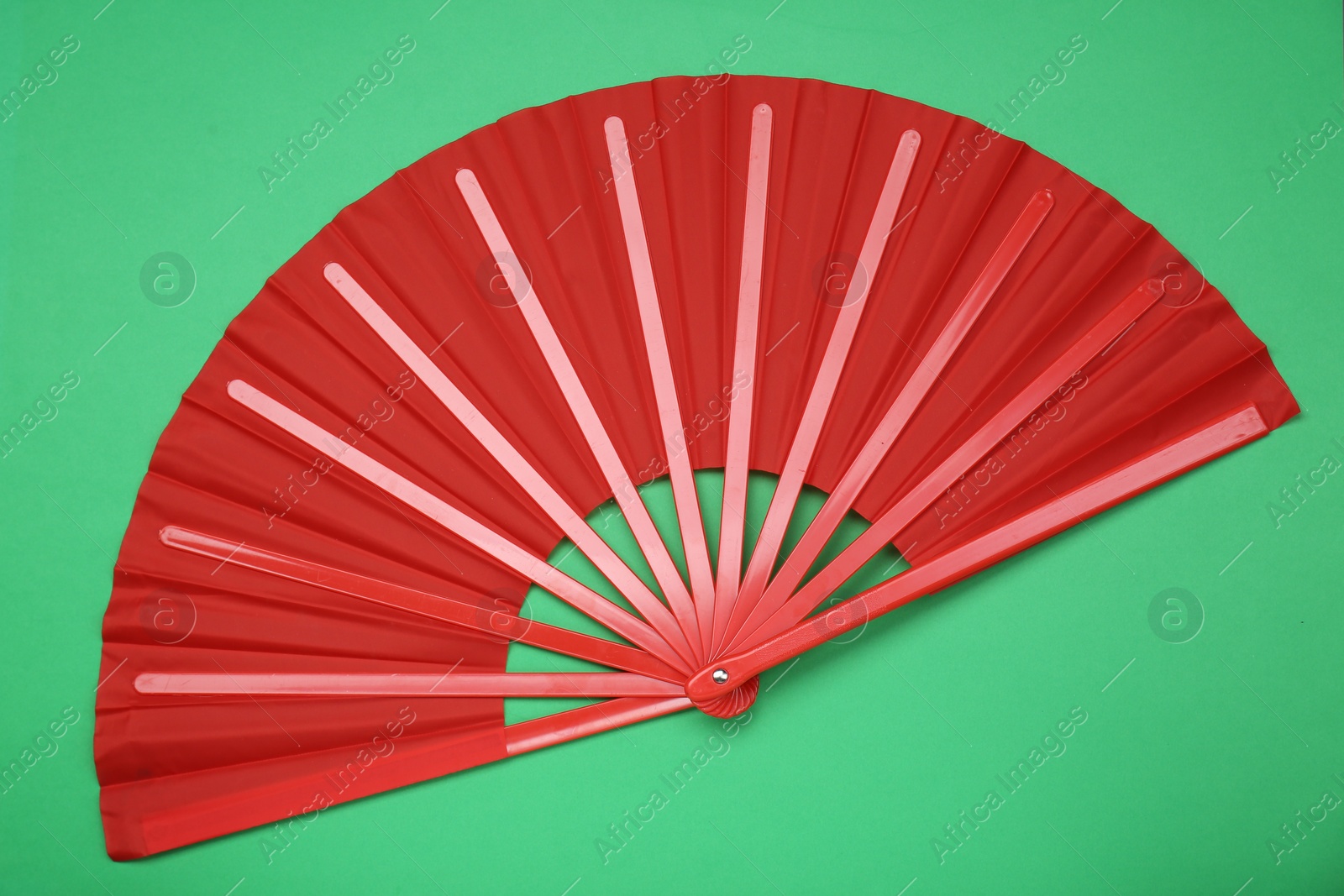 Photo of Bright red hand fan on green background, top view