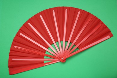 Bright red hand fan on green background, top view