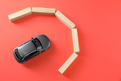 Photo of Development through barriers overcoming. Silver toy car movement blocked by wooden blocks on coral background, flat lay with space for text