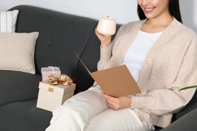 Photo of Happy woman reading greeting card while drinking coffee on sofa in living room