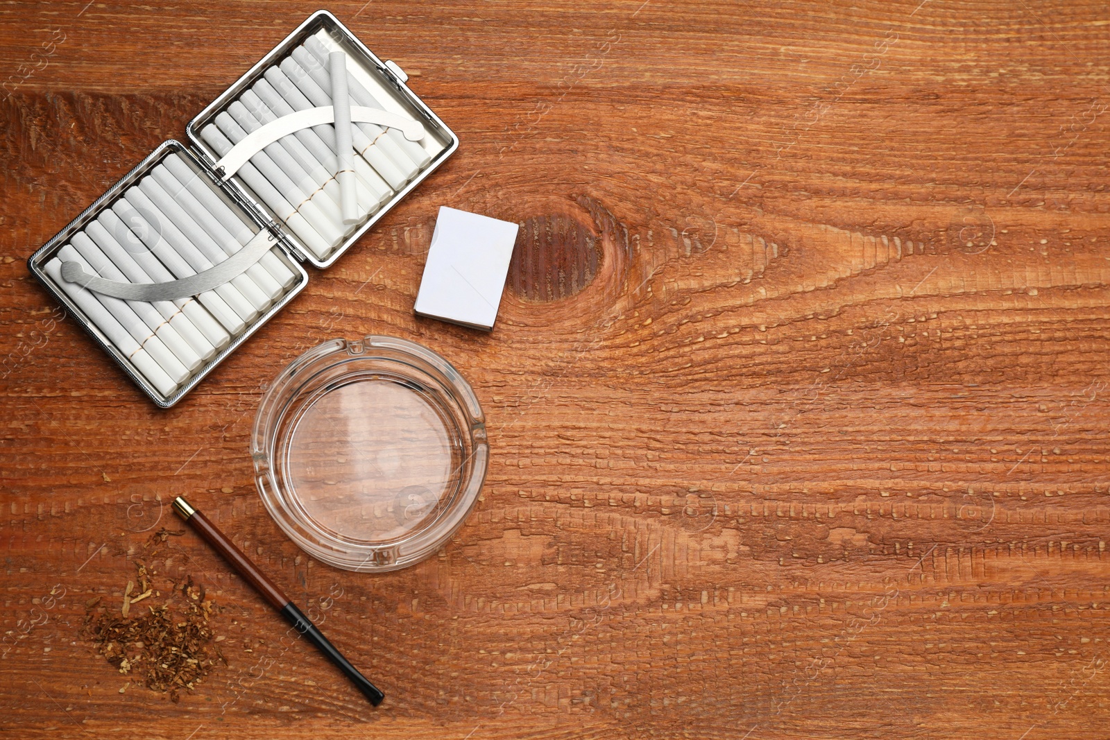 Photo of Cigarettes in case, holder, matchbox and ashtray on wooden table, flat lay. Space for text