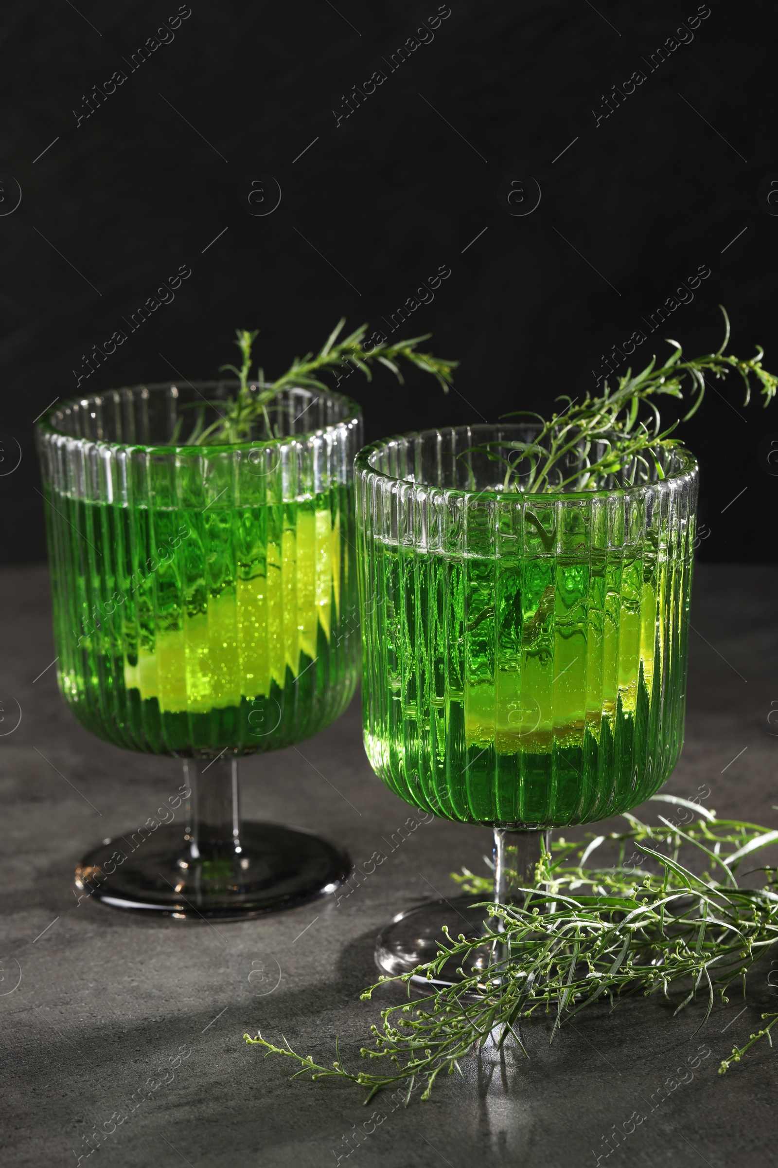 Photo of Glasses of homemade refreshing tarragon drink and sprigs on grey table